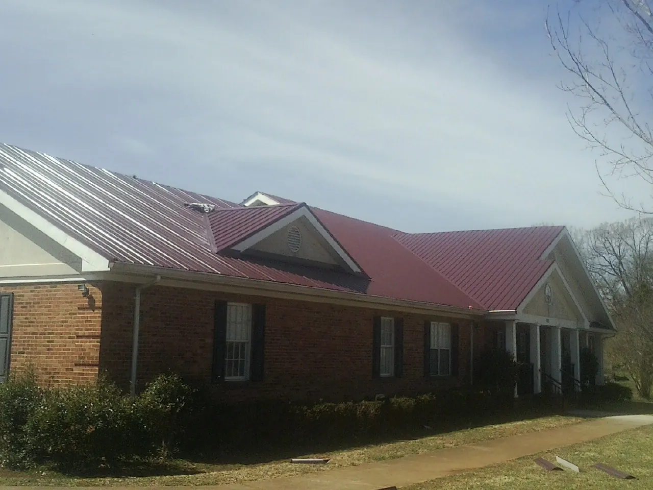Red metal roof with gabled entries on a long brick building, from a Hail Damage Roof Repair job in Newtown