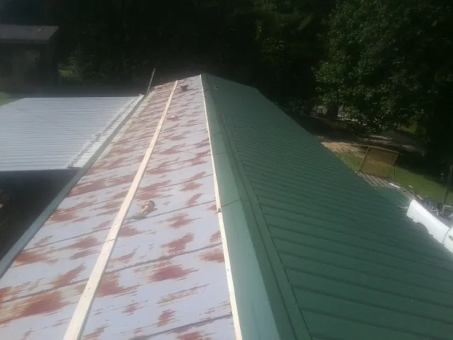 Old rusted panels beside newly installed green metal roofing — Wind Damage Roof Repair by Roofing Brothers in Newtown