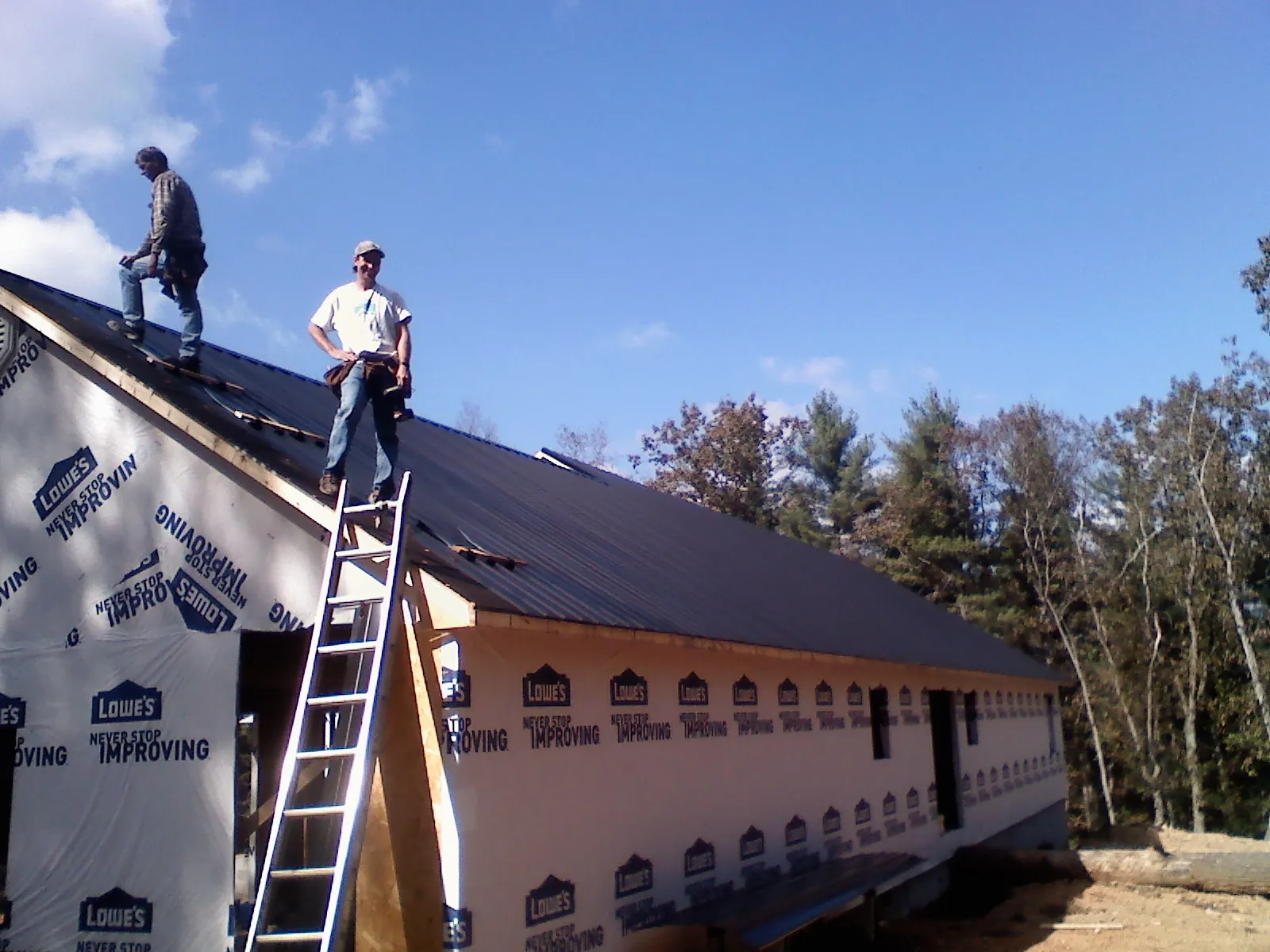 Two roofers standing on a long dark metal roof over a wrapped building in Newtown
